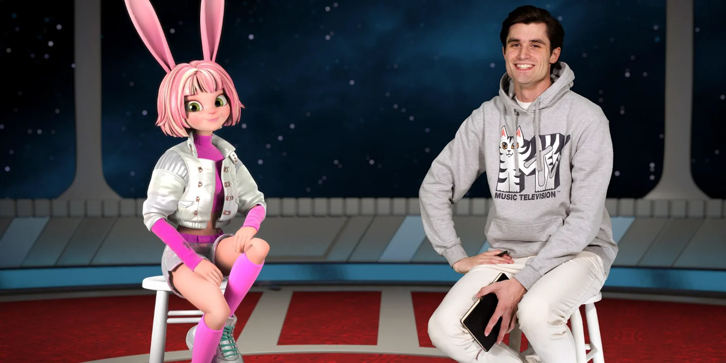 APOKI's rabbit artist persona seated beside a human host in the interview image published on the official artist site. The feature discusses GET IT OUT; this frame is not identified as a music-video still.